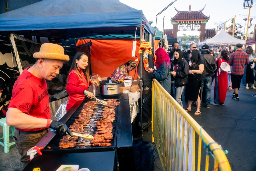 BBQ vendor grilling at DS Night Market with Chinatown gate in background